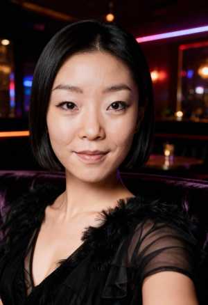 カラフルなライトを背景に薄暗い部屋に座っている、黒い薄手のドレスを着て毛皮のストール...。