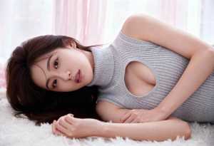 ふわふわの白い敷物の上に横たわり、カットアウトデザインのグレーのニットノースリーブト...。