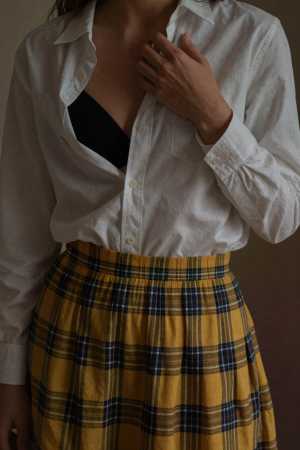 白いボタンダウン シャツと黄色のチェック柄のスカートを着た女性を、ローアングルの視点...。