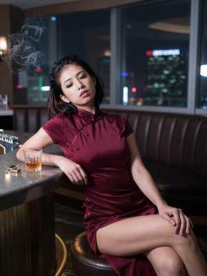 バーでウイスキーのグラスを前に座っている赤いチャイナ ドレスを着た女性を横から撮影し...。