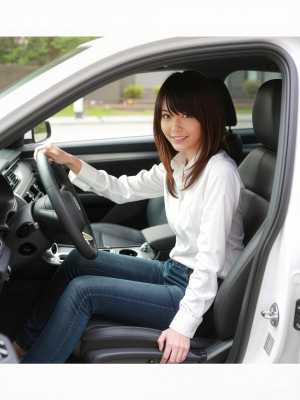 現代の車の運転席に座り、ハンドルを握りながら自信に満ちた笑みを浮かべている若い女性を...。