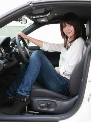 現代の車の運転席に座り、ハンドルを握りながら自信に満ちた笑みを浮かべている若い女性を...。