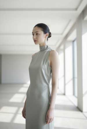 大きな窓のある空の部屋に立つ、ライトグレーのシルクドレスを着た若い女性を横顔カメラの...。