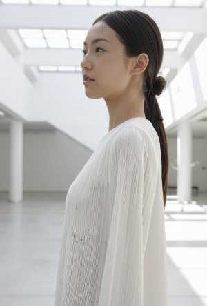 白い壁と大きな窓のあるモダンでミニマルな室内空間に立つ、長い黒髪を高い位置でポニーテ...。