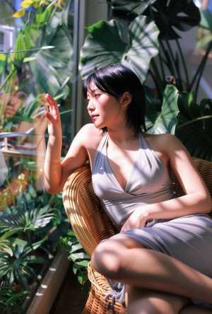 屋内で、豊かな緑に囲まれた籐の椅子に座っている若い女性を横顔カメラのアングルから写実...。