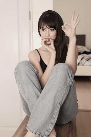 木製のベンチに足を組んで座り、「OK」のサインを出している若い女性を正面から写実的に...。