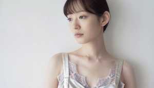 真っ白な壁を背景に撮影された、中性的な表情を持つ若い女性の写実的なポートレート。