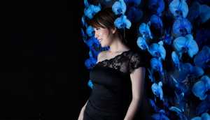 黒いドレスを着て、青い蘭の花の壁の前に立つ若い女性を横顔カメラのアングルから写実的に...。