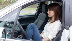 現代の車の運転席に座り、瞑想的な表情で窓の外を眺めているアジア系の若い女性。