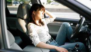 白いブラウスとブルー ジーンズを着て、現代の車の運転席に座っている若い女性を横から撮...。