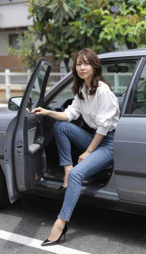 白いブラウスとブルー ジーンズを着て車の運転席に座っている若い女性を横から撮影した写...。