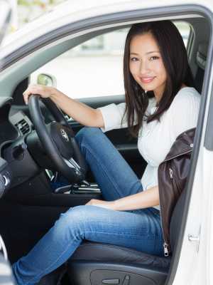現代の車の運転席に座り、カメラに向かって微笑むアジア系の若い女性。