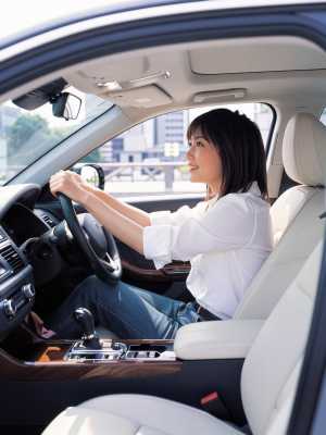 現代の車の運転席に座り、ハンドルを握りながら微笑む若い女性を正面から写実的に撮影したもの。
