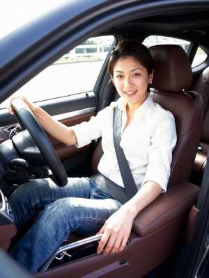 現代の車の運転席に座り、カメラに向かって自信に満ちた笑みを浮かべている若い女性。