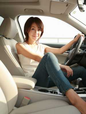現代の車の運転席に座り、ハンドルを握りながら自信に満ちた笑みを浮かべている若い女性を...。