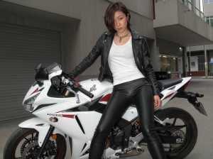 都市部でバイクの隣でポーズをとる若い女性を横から撮った写実的な写真。