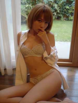 大きな窓の前の木の床に座り、白いレースのブラジャーとそれに合ったパンティーを身に着け...。