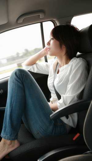 白いブラウスとブルー ジーンズを着て、車の中で座って思索にふける若い女性を横から撮っ...。
