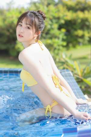 黄色いビキニを着てプールに立ち、肩越しに瞑想的な表情を浮かべている若い女性を横から撮...。