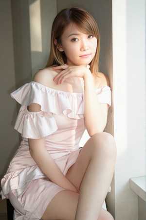 フリルの付いたピンクのオフショルダー ドレスを着て、明るい色の部屋で壁に向かって座っ...。