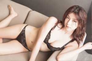 黒いレースのランジェリーを着て、ベージュのソファにリラックスしたポーズで横たわってい...。