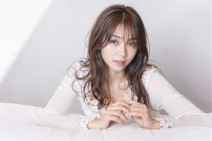 柔らかい中間色の部屋の白いベッドに横たわる、長くウェーブのかかった茶色の髪を持つ若い...。