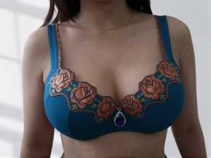 複雑な花柄の刺繍が施された青いブラジャーと涙滴型の宝石のペンダントを身に着けている女...。