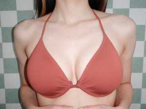 緑と白の市松模様の背景にサンゴ色のビキニトップを着た女性を正面カメラのアングルから写...。