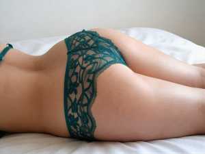 青緑のレースのTバックを履き、白いシーツを敷いたベッドに横たわる人物の裏側をローアン...。