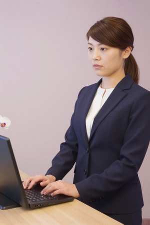 ホテル受付でPC作業と来客対応する女性