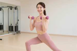 ジムでダンベルランジをする女性