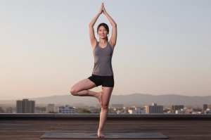 屋上でヨガの木のポーズをとる男性