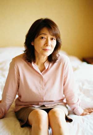 柔らかく暖かい光の中でベッドに座る中年のアジア人女性のポートレート。