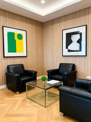 部屋の中央に 2 つの黒い革張りの椅子とガラスのコーヒー テーブルを備えたモダンなオ...。