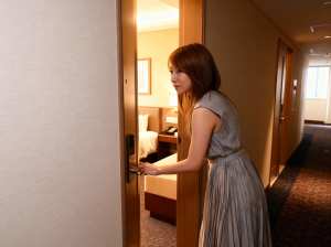 ホテルの一室で瞑想的な表情でドアを開ける若い女性を横から写実的に撮影した写真。