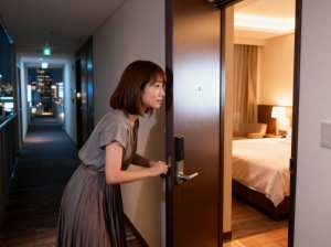 背景の窓から見える街のスカイラインを背景に、夜にホテルの部屋のドアを開ける若い女性を...。