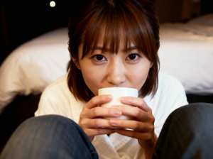 白いコーヒーカップを手に持ち、ベッドに座っている若い女性の接写写真。