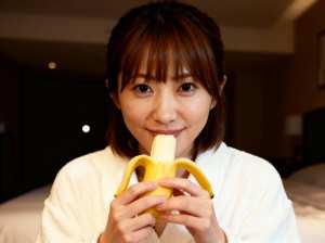 白いローブを着て、皮をむいたバナナを顔の前に持つ、短い茶色の髪のアジア系の若い女性の接写。