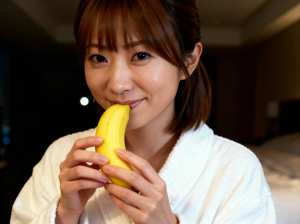 白いバスローブを着た、短い茶色の髪の若い女性が口の前に黄色いバナナを持っている接写写真。