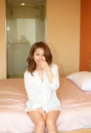 ガラスのドアを背景に、モダンな寝室のベッドに座っている若い女性を正面から写実的に撮影...。