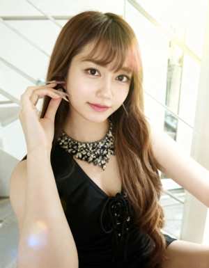 ウェーブのかかった茶色の長い髪と前髪を持ち、主張のあるネックレスが付いた黒いドレスを...。