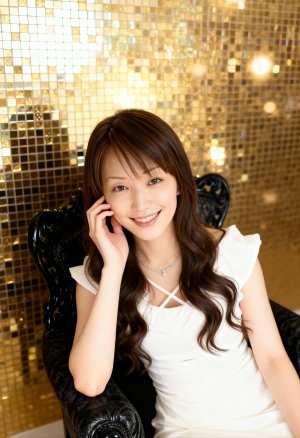 金のスパンコールの壁の前で黒い華やかな椅子に座り、カメラに向かって微笑む若い女性を、...。