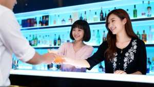 カラフルなアルコールのボトルを背景に、薄暗いバーのバーカウンターで握手する 2 人の...。