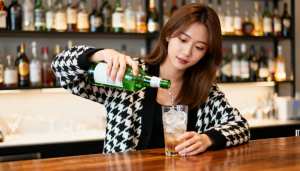 薄暗いバーの木製バーカウンターの上に、黒と白の千鳥格子柄のカーディガンを着た、長い茶...。