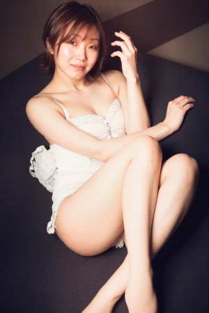 白いレースのドレスを着て、黒い表面にリラックスして座っている若い女性を横から撮った写...。