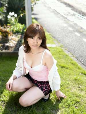 ピンクのタンクトップと花柄の短い黒のスカートを着て、カジュアルなポーズで草の上にしゃ...。