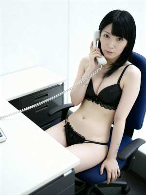 黒いレースのブラジャーとそれに合うパンティーを身に着け、机に座って電話で話している若...。