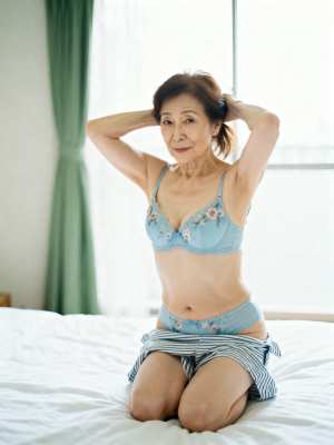 寝室のベッドに座るアジア系の年配の女性。