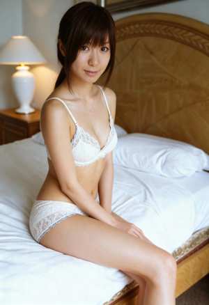 居心地の良い寝室でベッドに座り、白いレースのブラジャーとそれに合ったパンティーを身に...。