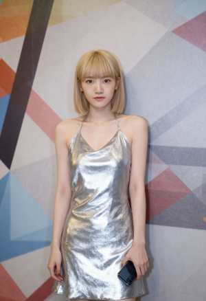 光沢のあるシルバーのドレスを着て、幾何学模様の壁の前に立っている若い女性を正面カメラ...。